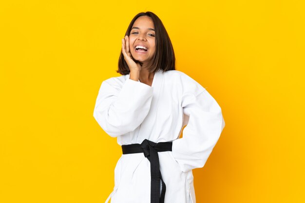 Mulher jovem fazendo caratê, isolada em um fundo amarelo, gritando com a boca aberta