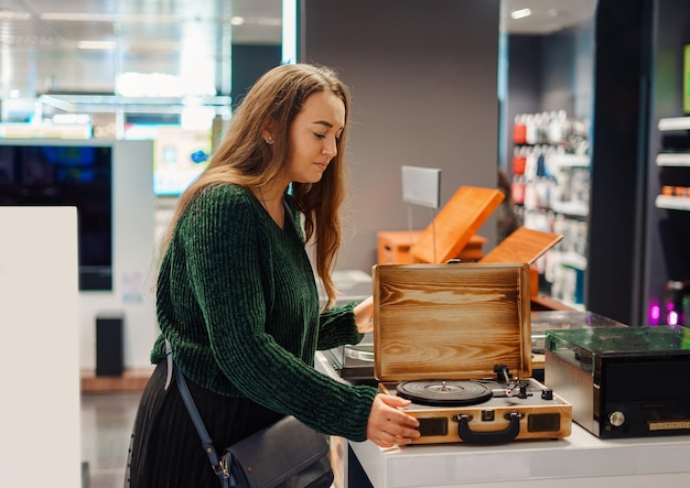 Mulher jovem fazendo compras em equipamentos musicais e loja de instrumentos musicais examina gramofone retrô