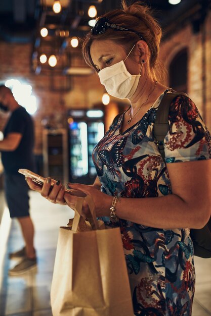 Foto mulher jovem fazendo compras na mercearia à noite usando a máscara facial para evitar a infecção por vírus