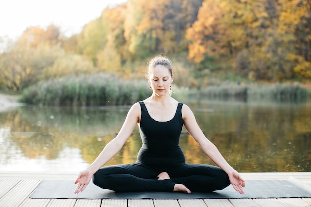 Mulher jovem fazendo ioga asana na natureza perto do lago