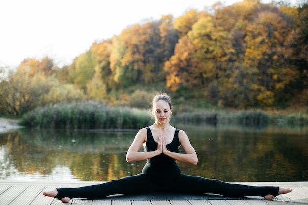 Mulher jovem fazendo ioga asana na natureza perto do lago