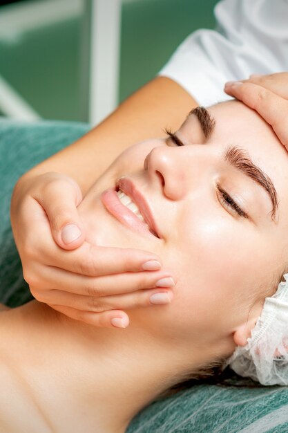 Mulher jovem fazendo massagem facial com os olhos fechados por uma esteticista em um salão de beleza