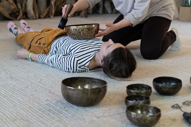 Mulher jovem fazendo massagem tibetana cantando terapia com pratos tradicionais de bronze tibetano em casa