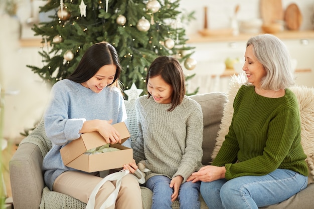 Mulher jovem feliz abrindo o presente de Natal enquanto está sentada no sofá com a família em casa