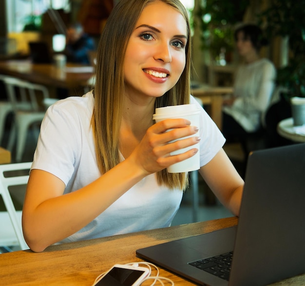 Mulher jovem feliz bebendo café e usando laptop