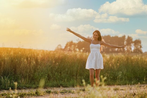 Mulher jovem feliz caminhando ao longo da estrada rural no prado durante o pôr do sol