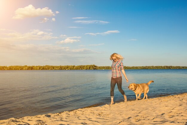 Mulher jovem feliz caminhando em uma praia com seu golden retriever no pôr do sol