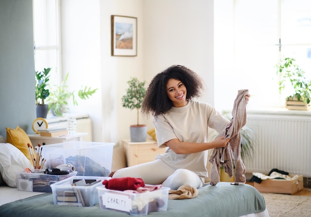 Mulher jovem feliz classificando roupas dentro de casa em casa, o conceito de doação de caridade.