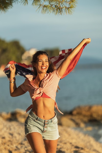 Mulher jovem feliz com bandeira nacional dos EUA se divertindo e passando o dia na praia.