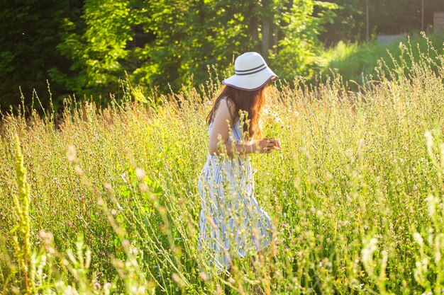 Mulher jovem feliz com cabelo comprido, usando chapéu e vestido puxando as mãos em direção às plantas