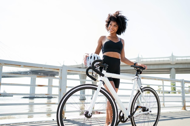 Mulher jovem feliz com cabelos cacheados em roupas esportivas andando de bicicleta na cidade Transporte ecológico