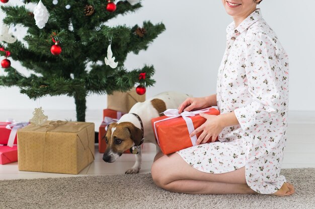 Mulher jovem feliz com cachorro adorável abrindo a caixa de presente sob a árvore de Natal. Conceito de férias.