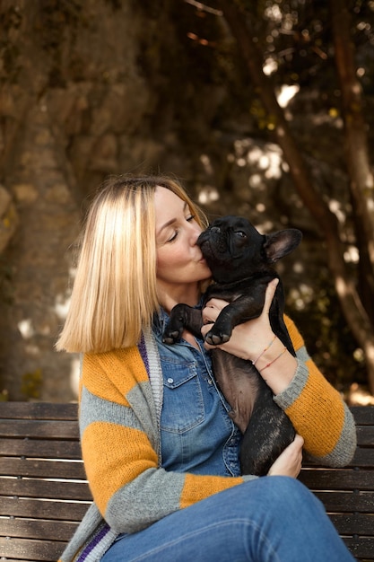 Mulher jovem feliz com cachorro bulldog francês sentado em um banco ao ar livre