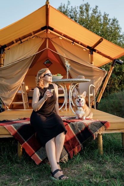 Mulher jovem feliz com cachorro Welsh Corgi Pembroke relaxando em glamping no dia de verão Barraca de acampamento de luxo para recreação ao ar livre e recreação Conceito de estilo de vida