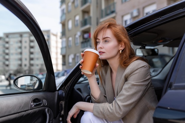 Mulher jovem feliz com café tendo um freio em seu carro vista lateral da mulher com café para ir na mão jovem mulher tomando café em seu carro