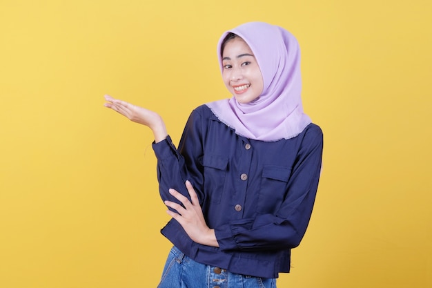 Mulher jovem feliz com expressão facial feliz mostra algo na mão usando hijab e roupas casuais em amarelo