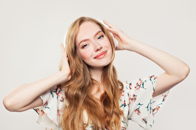 Mulher jovem feliz com fones de ouvido modelo ruiva ouvindo música em branco