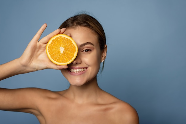 Mulher jovem feliz com meia laranja na frente do rosto, sobre fundo azul