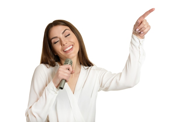 Mulher jovem feliz com microfone e apontando com o dedo sobre fundo branco