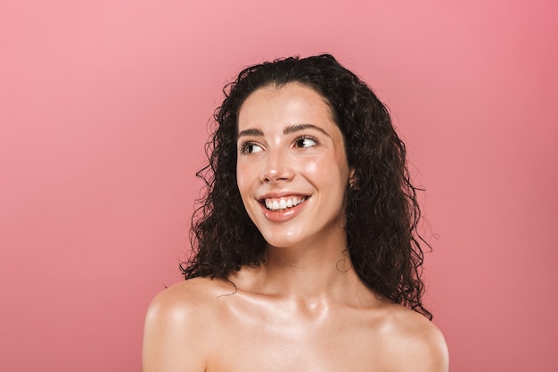 Mulher jovem feliz com pele saudável posando isolada sobre uma parede rosa.