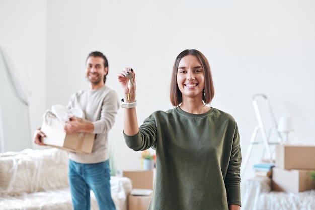 Mulher jovem feliz com um sorriso cheio de dentes mostrando a chave do novo apartamento ou casa