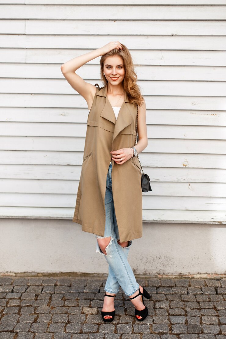 Foto mulher jovem feliz com um sorriso em roupas da moda com jeans e sapatos pretos com uma bolsa perto de uma parede de madeira