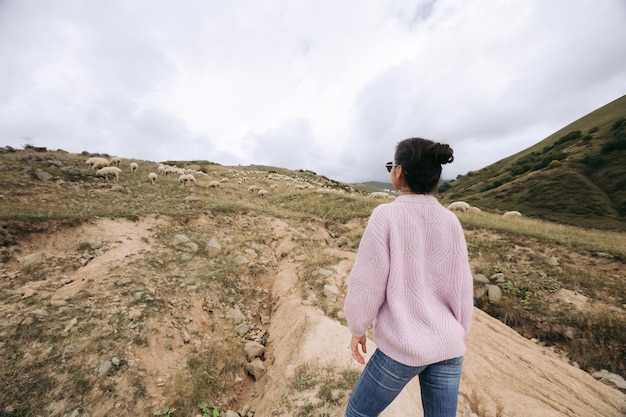 Foto mulher jovem feliz com um suéter contra rebanhos de ovelhas nas montanhas