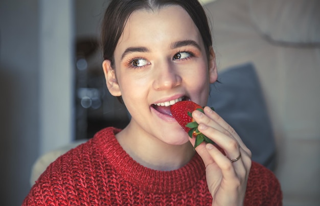 Mulher jovem feliz comendo morangos em casa