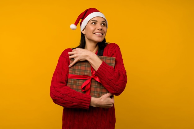 Foto mulher jovem feliz e animada com chapéu de papai noel com caixa de presente sobre fundo amarelo - imagem