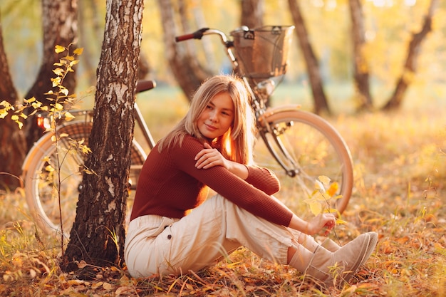 Mulher jovem feliz e ativa andando de bicicleta vintage no parque de outono ao pôr do sol