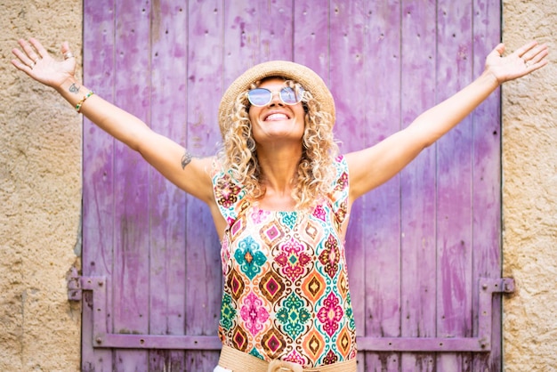 Mulher jovem feliz e muito feliz, abrindo os braços e olhando para cima com um sorriso Emoção alegre Mulher com roupas coloridas e estilo moderno, aproveite o estilo de vida Casa de parede ao fundo Prazer