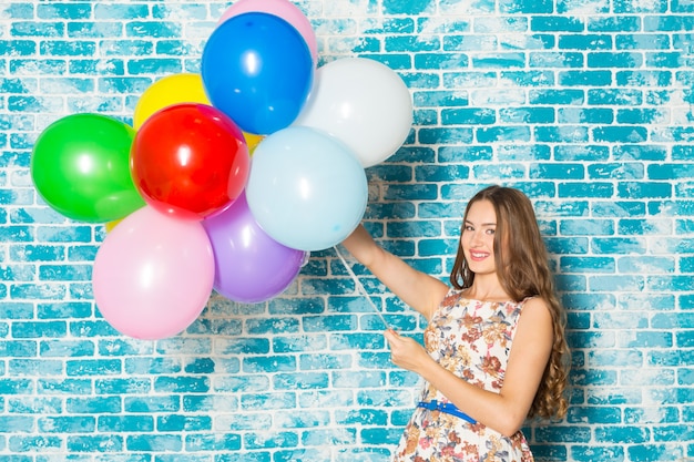 Mulher jovem feliz, em cima de parede azul e segurando balões