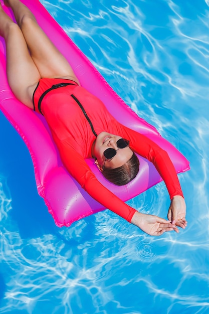 Mulher jovem feliz em óculos de sol e biquíni rosa flutuando no colchão inflável à beira da piscina Conceito de férias de verão Viajar por mar