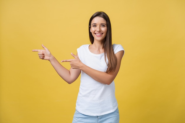 Mulher jovem feliz em pé e apontando o dedo no espaço de cópia isolado sobre o fundo da parede de ouro amarelo olhando a câmera