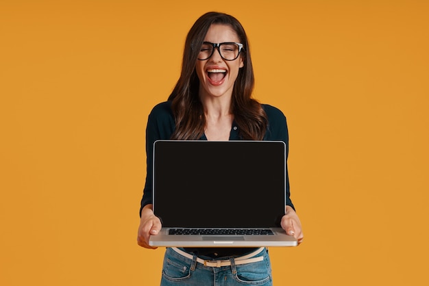 Mulher jovem feliz em roupas casuais elegantes, apontando para o espaço da cópia no laptop