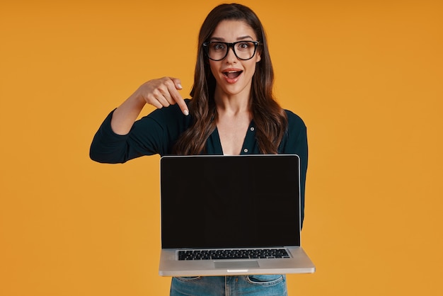 Mulher jovem feliz em roupas casuais elegantes, apontando para o espaço da cópia no laptop