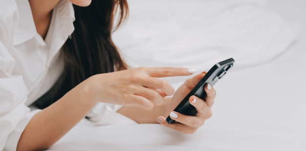 Mulher jovem feliz em roupas casuais sorrindo e olhando para a câmera enquanto usa laptop na cama no quarto em casa