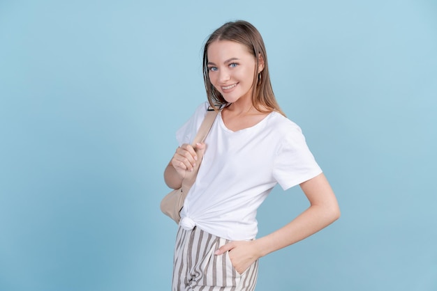 Mulher jovem feliz em roupas leves com mochila nas costas posando no estúdio