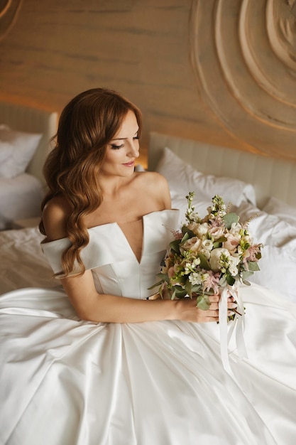 Foto mulher jovem feliz em um vestido de noiva desfrutando com um buquê de noiva na cama