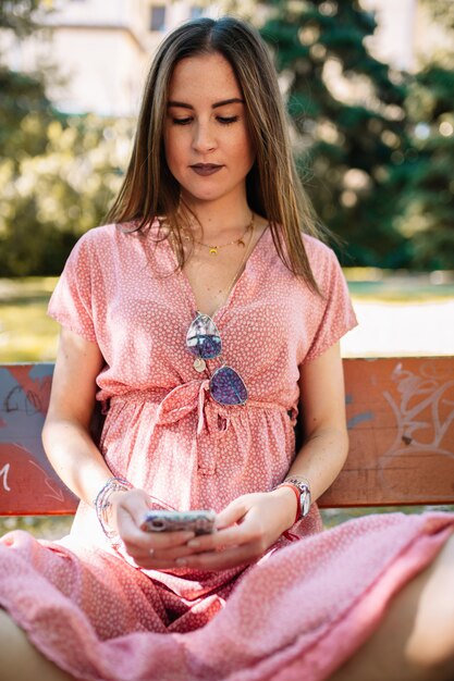 Mulher jovem feliz em um vestido rosa, sentado num banco assistindo móvel. Mulher tendo boas notícias. Mulher ilusória