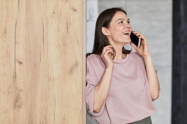 Mulher jovem feliz encostada na parede falando no celular e rindo durante a conversa