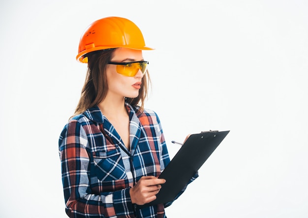 Mulher jovem feliz está usando capacete de segurança laranja e camisa quadriculada, lendo as notas da área de transferência.