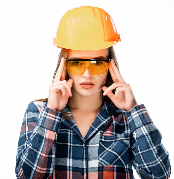 Mulher jovem feliz está usando capacete de segurança laranja, óculos amarelos e camisa quadriculada