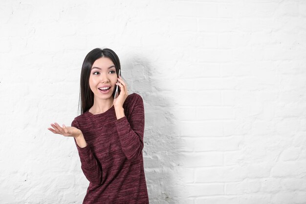 Mulher jovem feliz falando no celular perto de uma parede branca