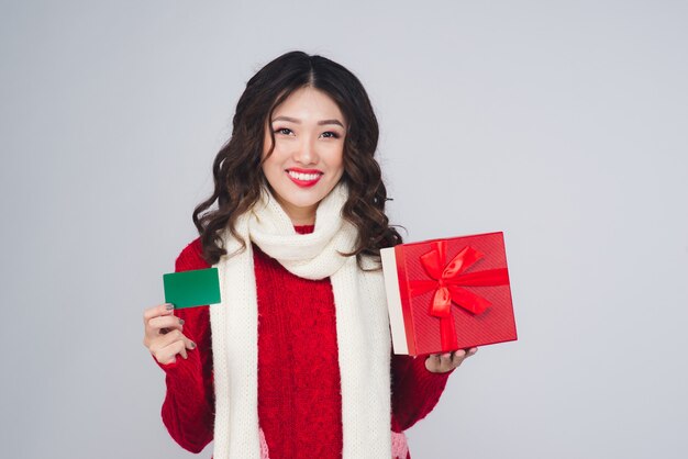 Mulher jovem feliz fazendo compras com cartão de crédito e segurando a caixa de presente no Natal isolado.