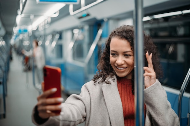 Mulher jovem feliz fazendo uma chamada de vídeo em pé no metrô