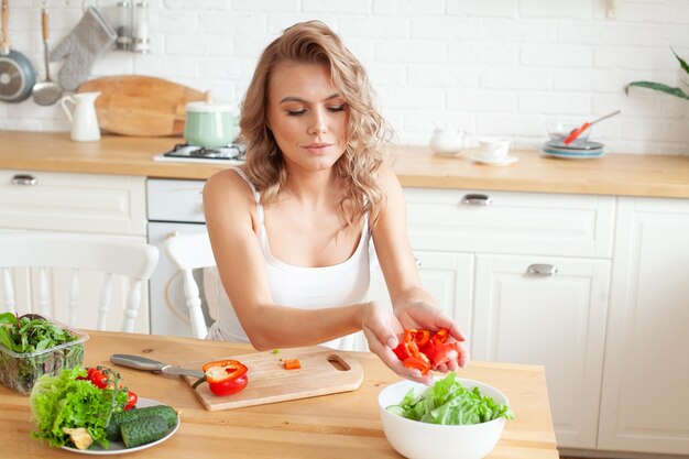 Mulher jovem feliz fazendo uma salada na cozinha