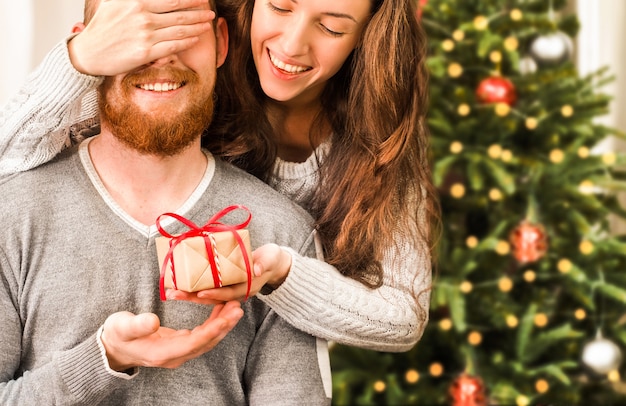 Mulher jovem feliz fecha os olhos do homem e lhe dá um presente de Natal