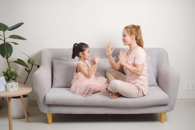 Mulher jovem feliz jogando jogo de bater palmas com criança do sexo feminino enquanto está sentado na sala de estar