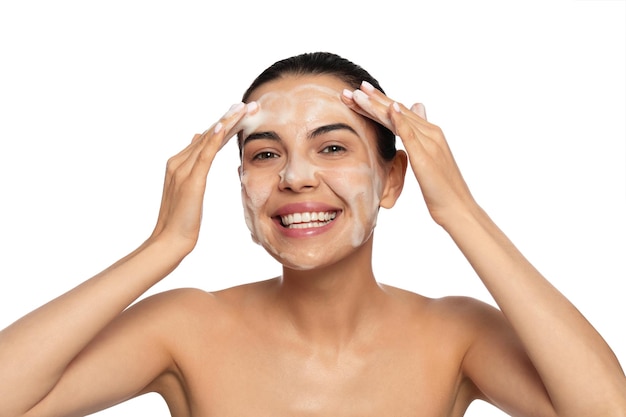 Mulher jovem feliz lavando rosto com produto cosmético em fundo branco
